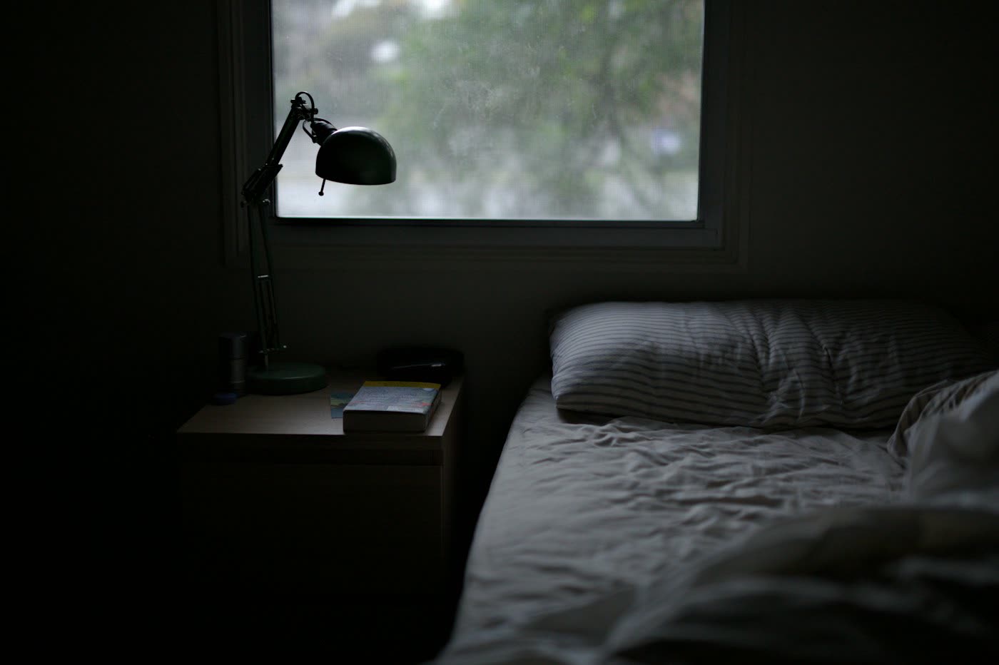 Dunkles, schlichtes Schlafzimmer mit Bett, Nachttisch mit Buch und Fenster
