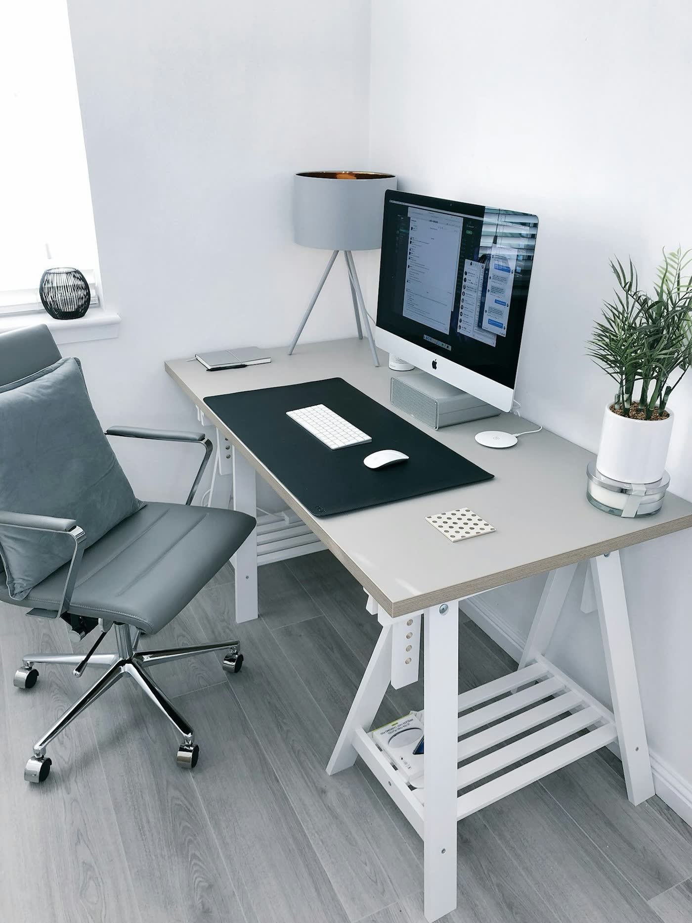 Heimarbeitsplatz mit Bürostuhl, hellem Tisch, Bildschirm, Lampe und Zimmerpflanze